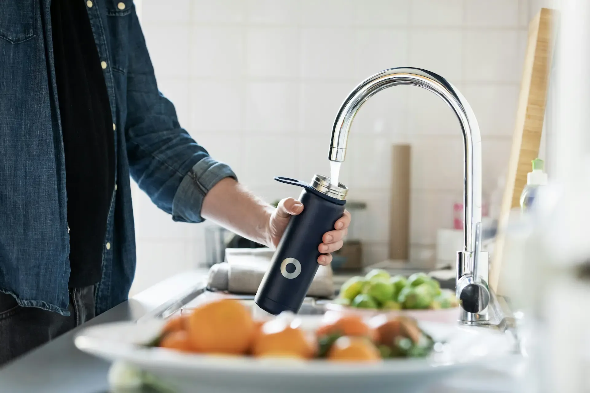 A man filling up a drink container at the kitchen tap