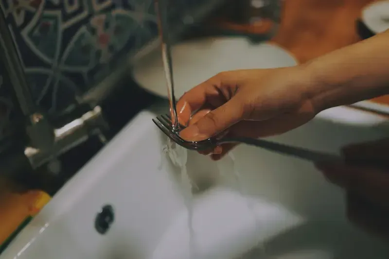 A person rinsing a fork under a running tap