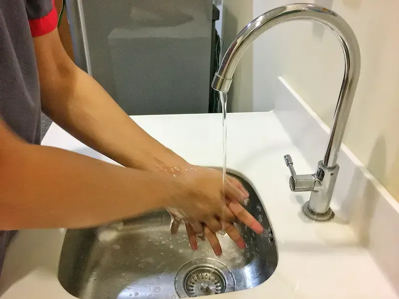 A person washing their hands in the kitchen sink